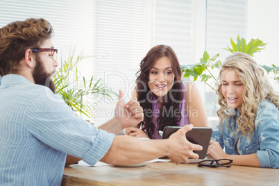 Man showing digital tablet to happy coworkers at desk