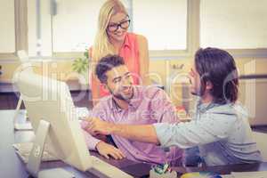 Businessman pointing on computer as smiling colleagues looking a