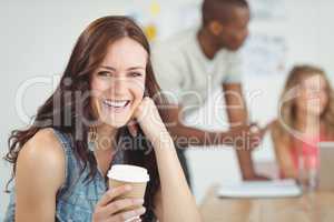 Portrait of smiling woman holding coffee cup while sitting at de