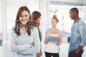 Portrait of smiling woman with arms crossed while coworkers disc