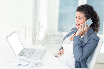 Pregnant businesswoman touching her belly while talking on mobil