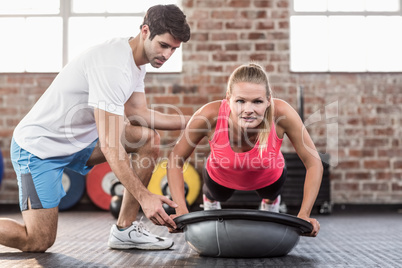 Trainer assisting woman with push ups at gym