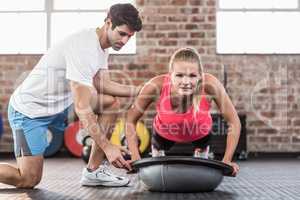 Trainer assisting woman with push ups at gym