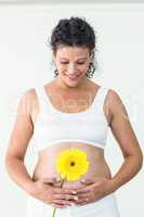 Happy pregnant woman touching her stomach while holding yellow f
