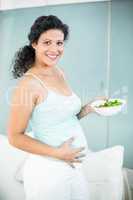 Pregnant woman touching her belly while holding bowl of salad