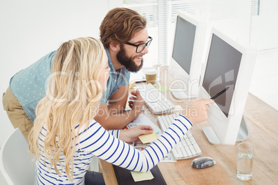 Woman pointing at computer with stylus while sitting by man