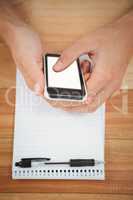 Man using smartphone with notepad on table in office