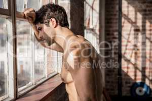 Shirtless man looking outside window