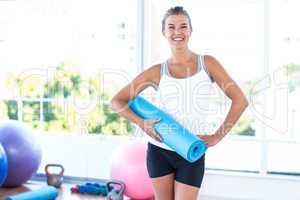 Woman smiling and holding yoga mat with hand on hip