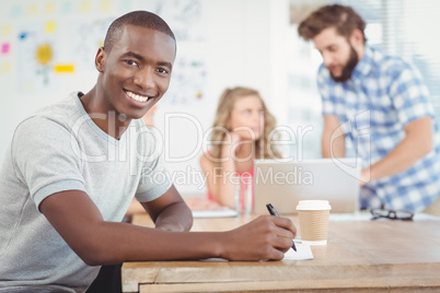 Portrait of smiling man writing on paper while sitting at desk