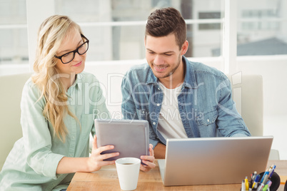 Smiling woman wearing eyeglasses showing digital tablet to man