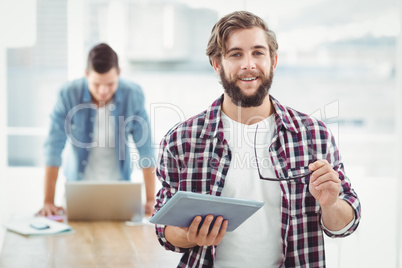 Portrait of smiling businessman holding eyeglasses and digital t