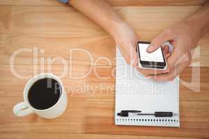 Hipster using smartphone with coffee and notepad on table in off
