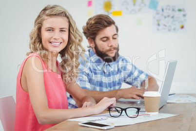 Portrait of smiling woman with man working on laptop