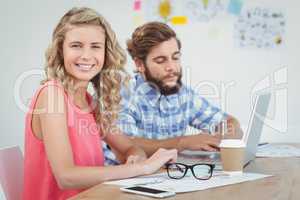 Portrait of smiling woman with man working on laptop