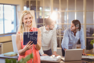 Smiling businesswoman using digital PC with male colleagues work