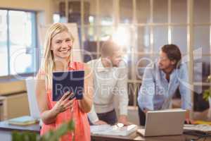 Smiling businesswoman using digital PC with male colleagues work