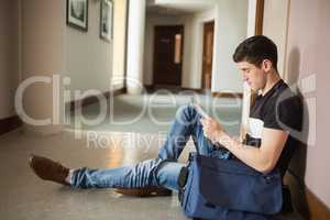 Male student using digital tablet sitting by wall