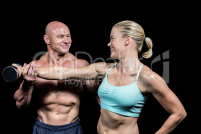 Cheerful trainer helping woman for lifting dumbbell