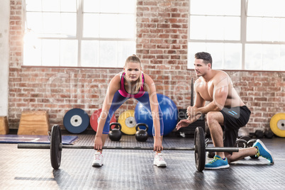 Woman lifting barbell with her trainer at crossfit session
