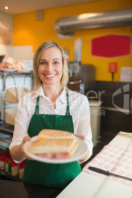 Happy female shop owner serving sandwich