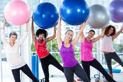 Portrait of smiling women holding exercise balls with arms raise