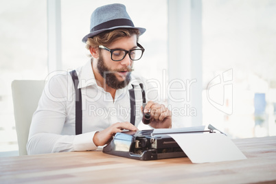 Hipster holding smoking pipe while working on typewriter
