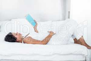 Pregnant woman reading a book while lying on a bed