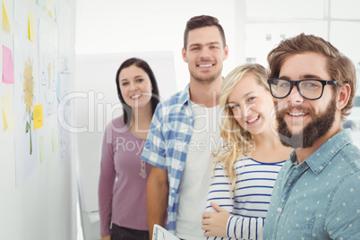 Portrait of smiling business people by wall with sticky notes an