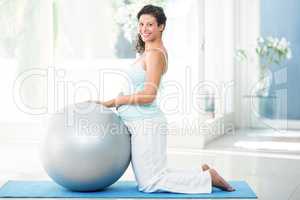 Pregnant woman with exercise ball kneeing on mat