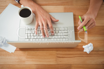 Man with coffee and pen working on laptop at desk in office