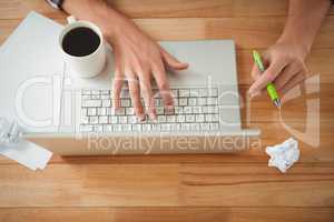 Man with coffee and pen working on laptop at desk in office