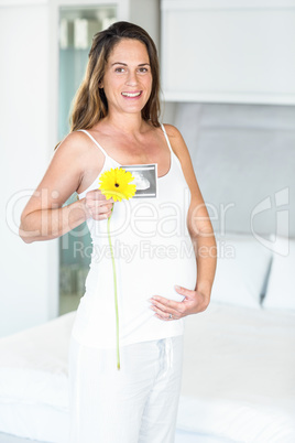 Portrait of happy pregnant woman with flower and ultrasound scan