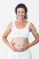Smiling pregnant woman listening to music while touching her bel