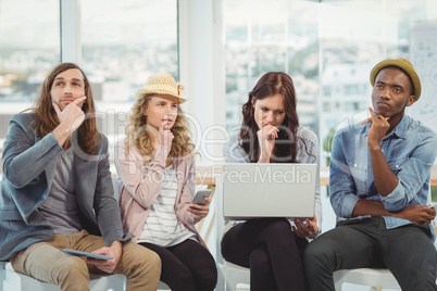 Thoughtful business people with hand on chin while sitting on ch