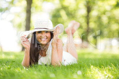 Happy woman holding sun hat while lying on grassland