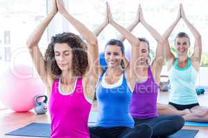 Women sitting in fitness studio with hands joined overhead