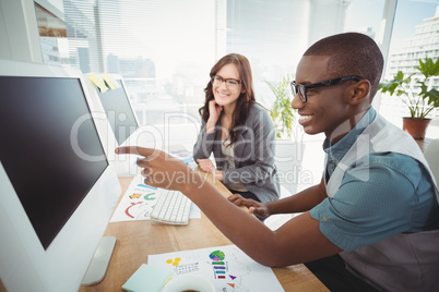 Businessman pointing at computer while sitting with coworker at