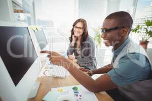 Businessman pointing at computer while sitting with coworker at