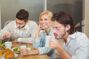 Businesswoman with male colleagues having snacks and coffee in c