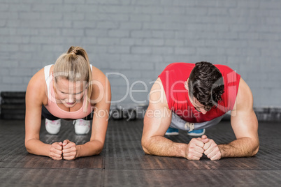 Fit smiling couple planking together in gym