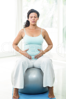 Pregnant woman with eyes closed touching her belly while sitting