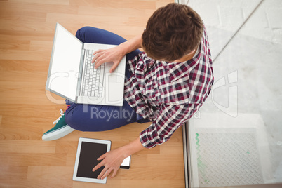 Hipster sitting with laptop on top while using digital tablet