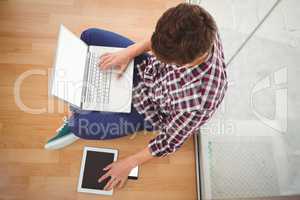 Hipster sitting with laptop on top while using digital tablet