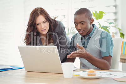 Businessman gesturing while discussing with coworker at desk