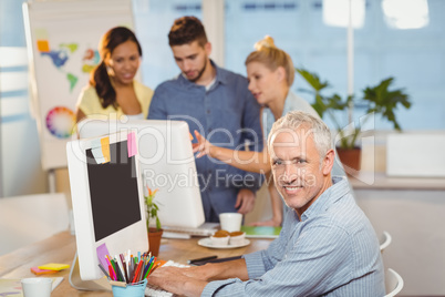 Confident businessman using on computer with colleagues in backg