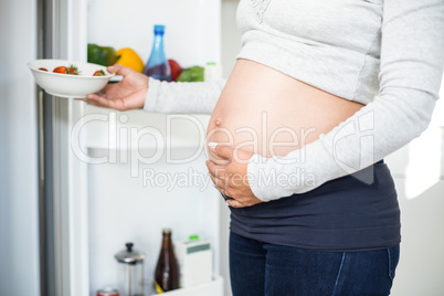 Pregnant woman keeping strawberries in fridge while touching bel