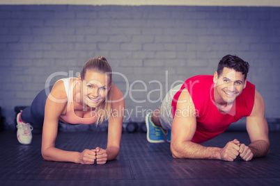 Fit smiling couple planking together in gym