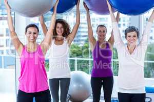 Portrait of cheerful women holding exercise balls with arms rais