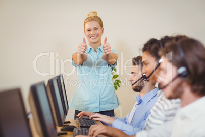 Businesswoman with thumbs up standing at employees